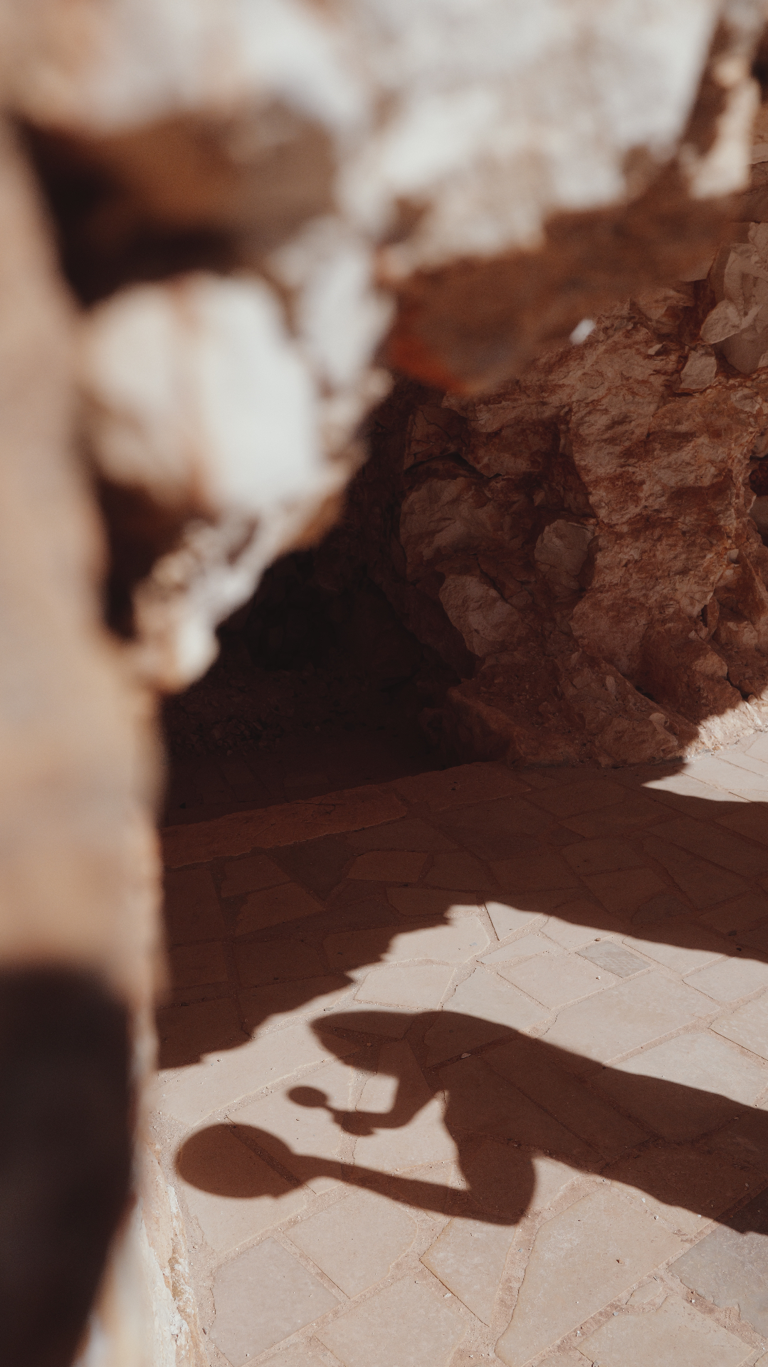 Shadow of a person drumming cast across the warm stone floor of the cave