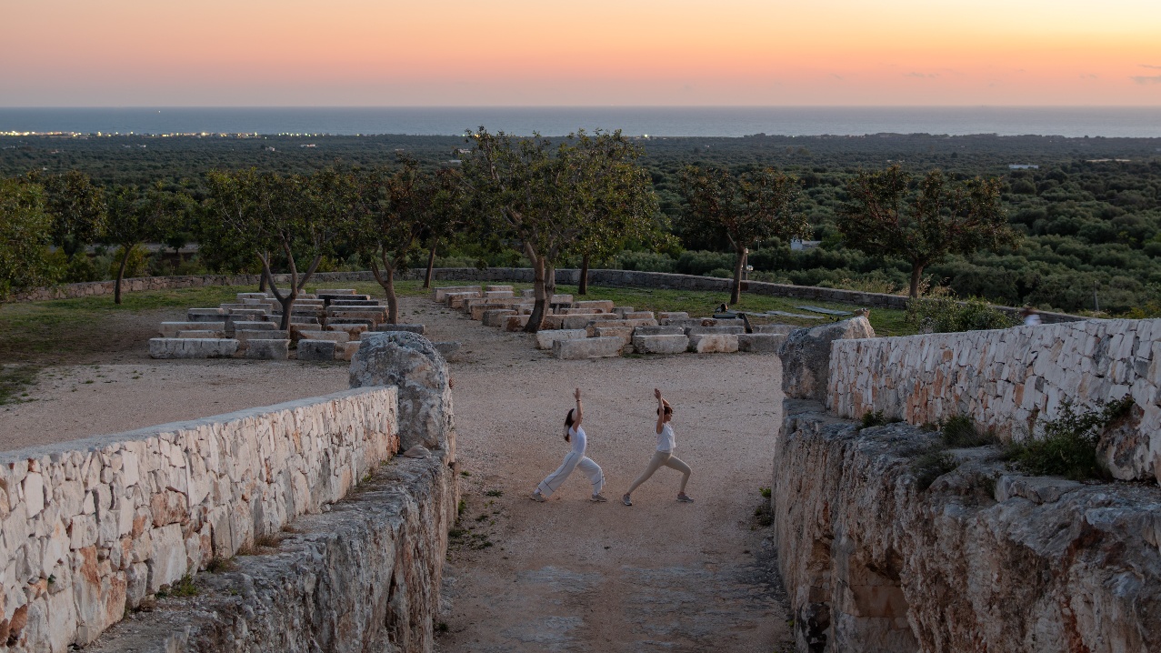 Two guests practicing yoga at sunset in the Cava Puglia stone amphitheatre
