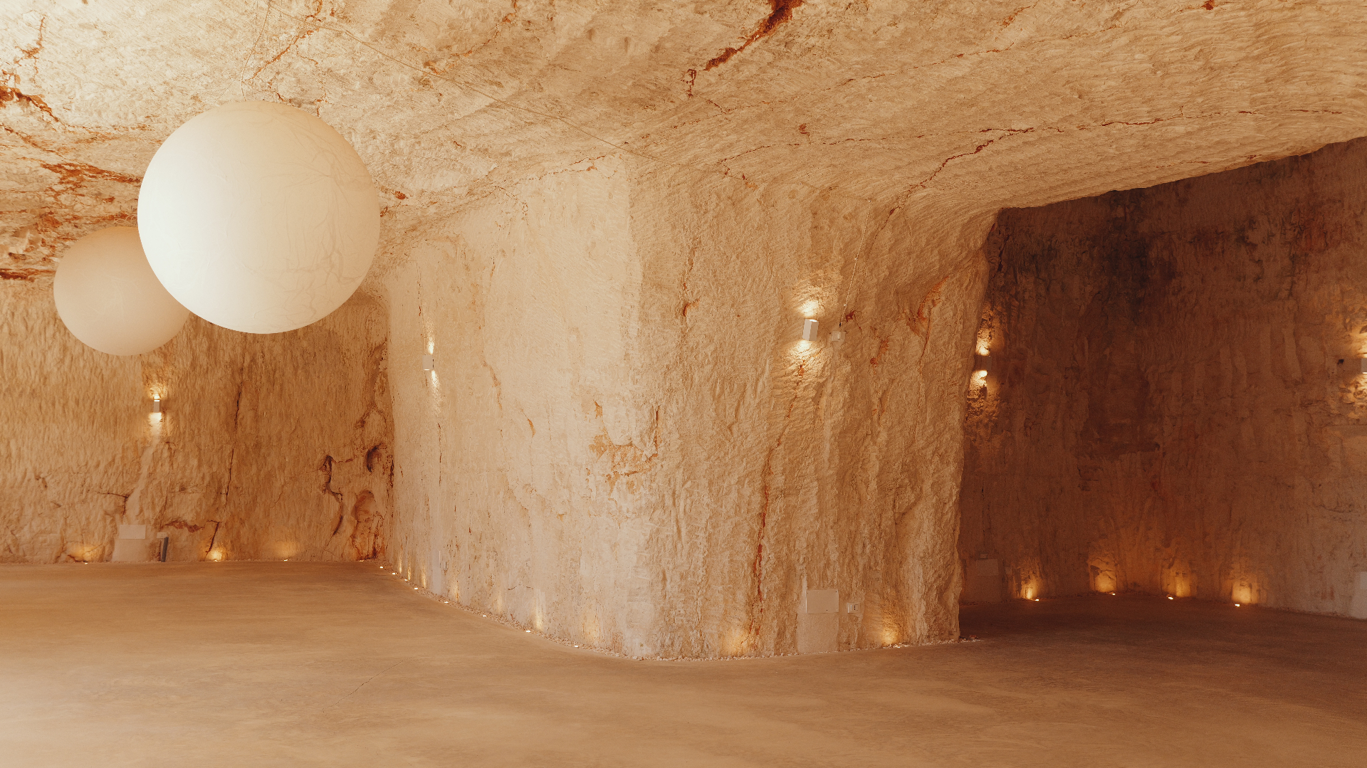 The white stone cave hall in Ostuni, illuminated by suspended paper moons and warm uplighting