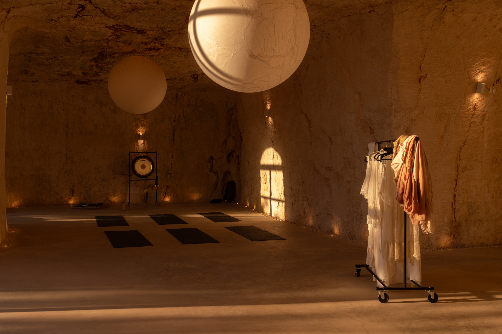 The cave studio at Cava Puglia with hanging paper moons, gong and yoga mats laid out on the stone floor